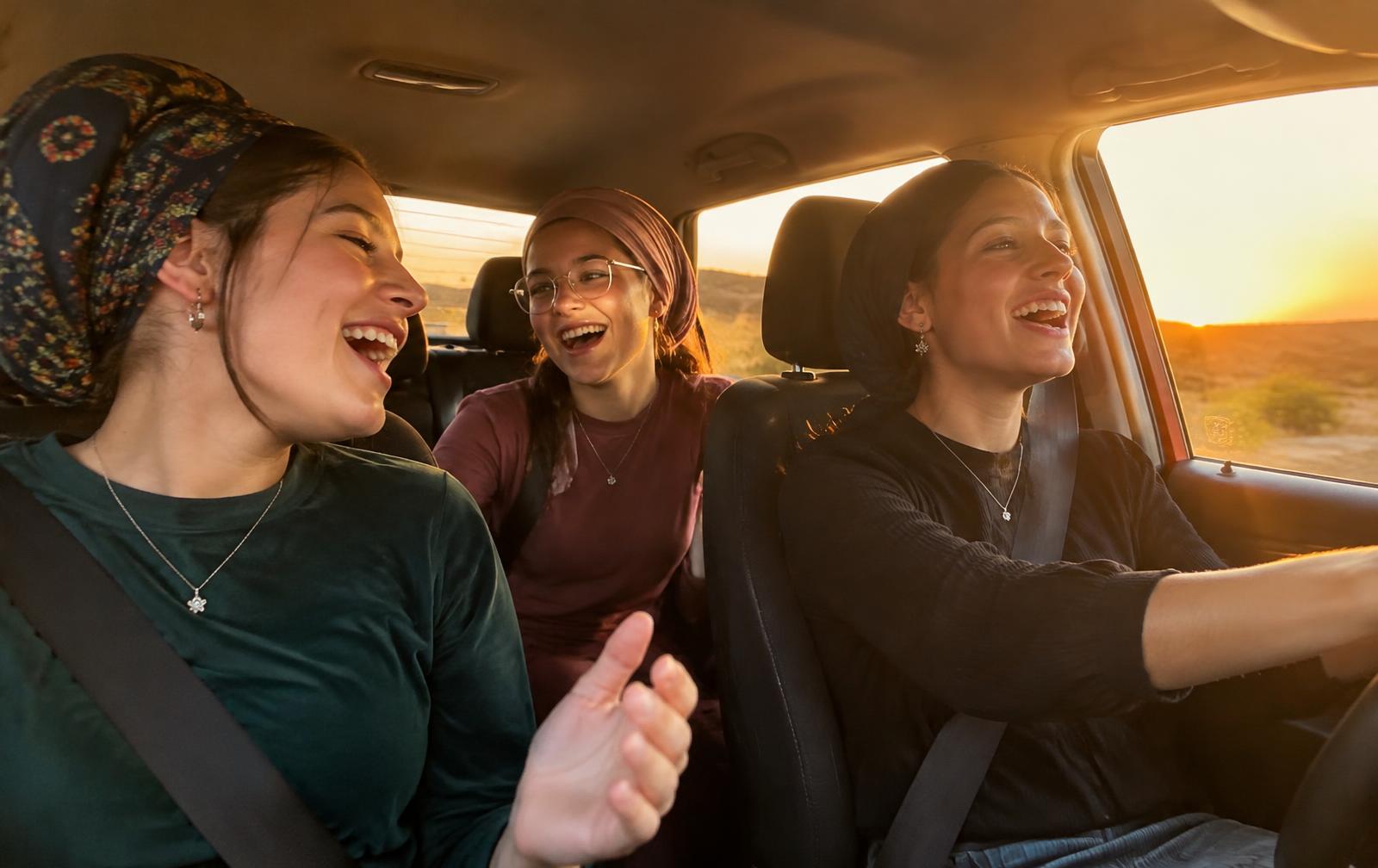 Three friends singing together in a car at sunset